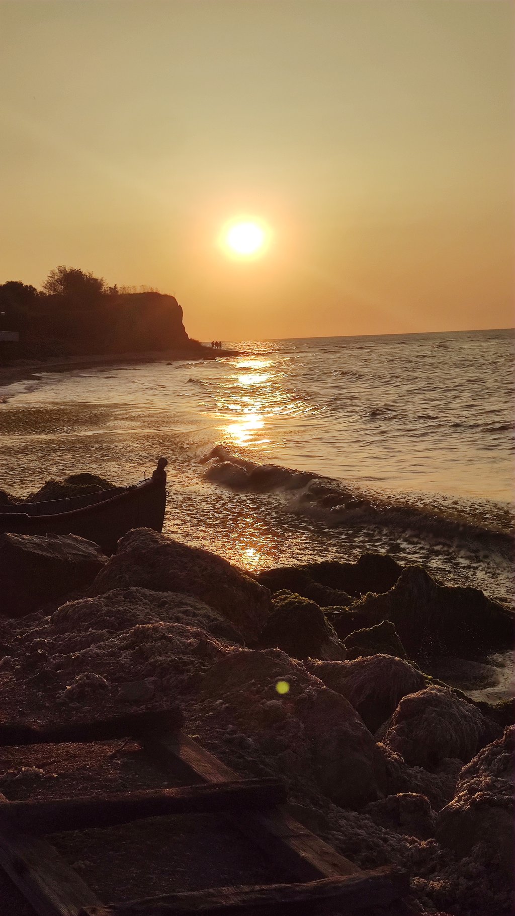 A silhouette of a person standing by the sea during a serene sunset, reflecting on the water's surface.