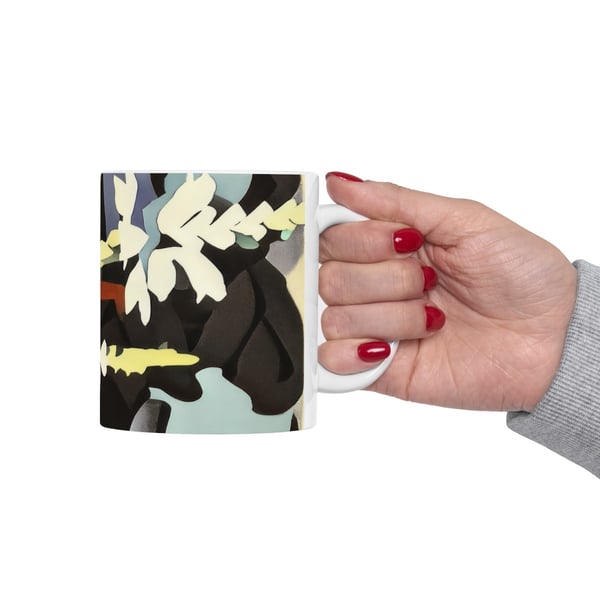 A close-up of a hand with red nails holding a white mug printed with a digital artwork of abstract botanical shapes in soft earth tones, reflecting a Montessori-inspired approach to art.