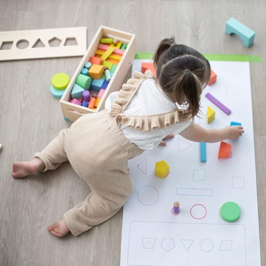 Child engaging with colorful wooden shapes and matching them on a large sheet of paper.