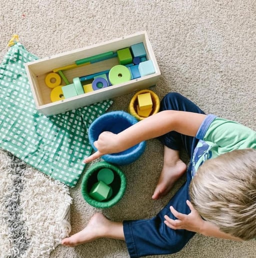 Child playing with colorful wooden blocks and sorting bowls on a carpet.